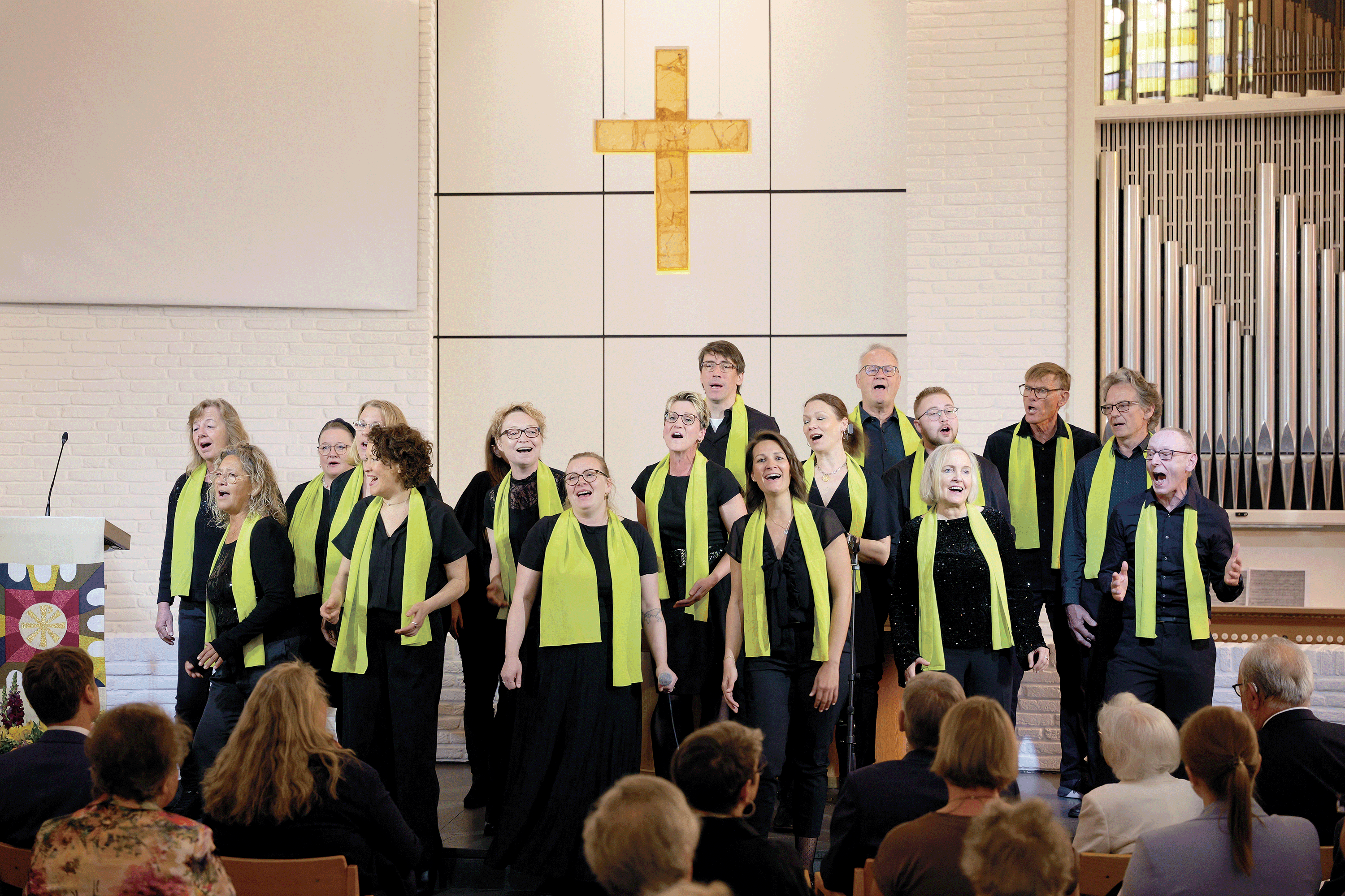 Die Mitglieder des Albertinen-Mitarbeitenden-Gospelchors singen bei einem Gospelkonzert auf der Bühne der Kiche beim Albertinen Krankenhaus in festlicher schwarzer Kleidung mit grünen Schals.