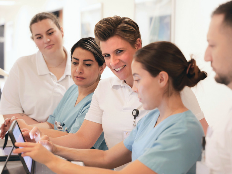 Zentrumsleiterin Dr. med. Julia M. Reinke blickt in die Kamera und steht mit einem Team am Stationswagen mit einem Tablet-Computer im auf Hüftprothesen, Knieprothesen und Schulterprothesen spezialisierten Albertinen Endoprothetikzentrum Hamburg