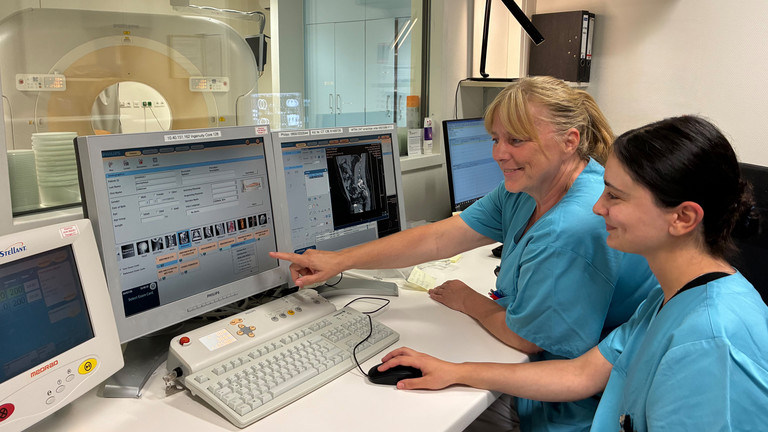 Zwei MTRs in blauen Kasacks sitzen vor mehreren PC Bildschirmen im Albertinen Krankenhaus, im Hintergrund ist ein CT-Gerät zu sehen Zwei MTRs in blauen Kasacks sitzen vor mehreren PC Bildschirmen im Albertinen Krankenhaus, im Hintergrund ist ein CT-Gerät zu sehen