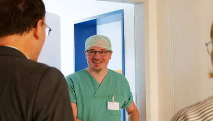 Eine OP-Pflegekraft in grüner Funktionskleidung und Kopfhaube unterhält sich auf dem Flur mit einem Mitarbeiter am Internationalen Tag der Pflegenden im Evangelischen Amalie Sieveking Krankenhaus in Hamburg.