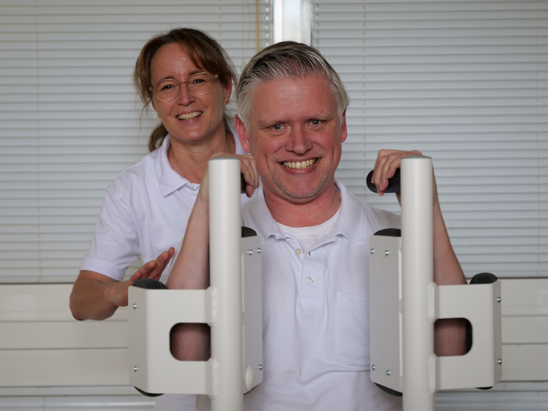 Ein Therapeut sitzt an einer speziellen Trainingsmaschine für Schulter- und Rückentraining in Begleitung einer Therapeutin bei Physikofit im Interdisziplinären Therapiezentrum für Physiotherapie im Albertinen Krankenhaus in Hamburg