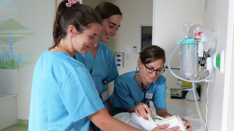 Drei Hebammen kümmern sich um ein neugeborenes Baby