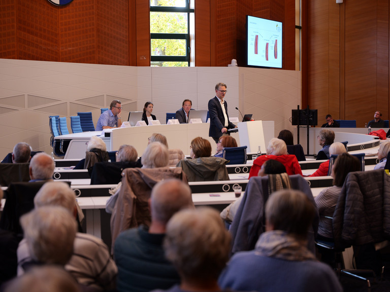 Blick über die Zuschauerreihen aufs Podium mit dem Chefarzt der Kardiologie am Standort Hamburg-Schnelsen Prof. Karsten Sydow beim 2. Norderstedter Herz- und Gefäßtag mit dem Albertinen Herz- und Gefäßzentrum Hamburg im Norderstedter Rathaus