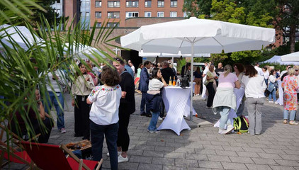 Blick auf einen großen weißen Sonnenschirm mit Stehtischen beim Albertinen-Sommerfest für die Mitarbeitenden aus den unterschiedlichen Einrichtungen der Immanuel Albertinen Diakonie am Standort Schnelsen auf dem Platz vor der Kirche am Albertinen Krankenhaus.