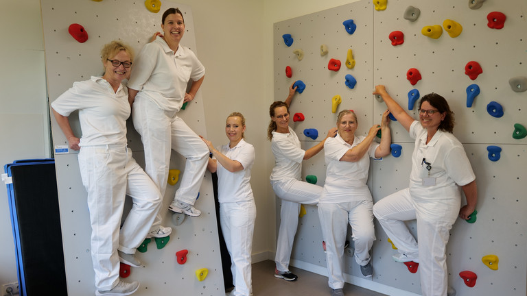 Mehrere Therapeutinnen in weißer Arbeitskleidung blicken an einer Kletterwand in die Kamera im Interdisziplinären Therapiezentrum des Albertinen Krankenhauses in HamburgMehrere Therapeutinnen in weißer Arbeitskleidung blicken neben und an einer Kletterwand in die Kamera im Interdisziplinären Therapiezentrum des Albertinen Krankenhauses in Hamburg