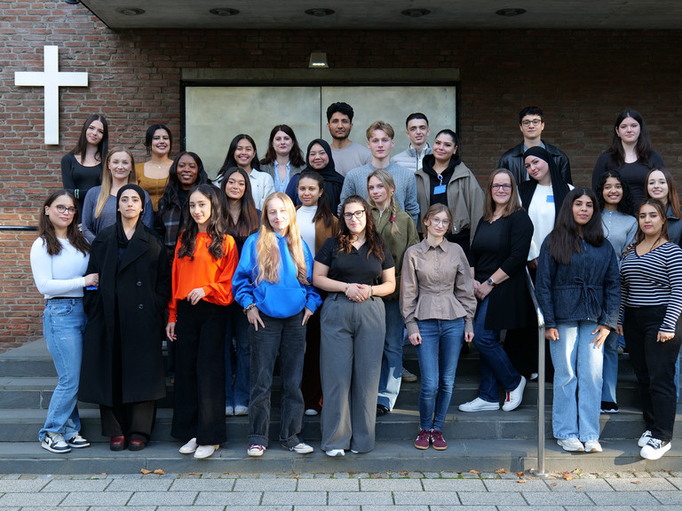 Gruppenfoto der neuen Pflege-Auszubildenden des Albertinen Krankenhauses auf einer Treppe vor dem Gebäudeeingang. Die Auszubildenden stehen in mehreren Reihen nebeneinander und blicken in die Kamera.