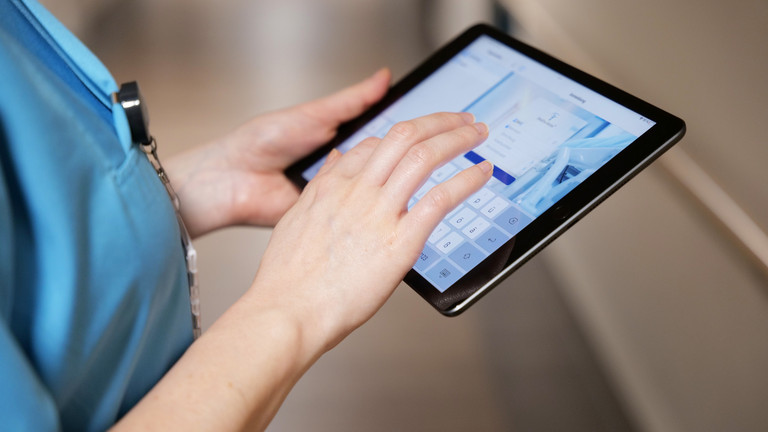 Blick auf ein digitales Tablet zur digitalen Dokumentation und Information in den Händen einer Pflegekraft in blauer Funktionskleidung im Albertinen Krankenhaus in Hamburg.