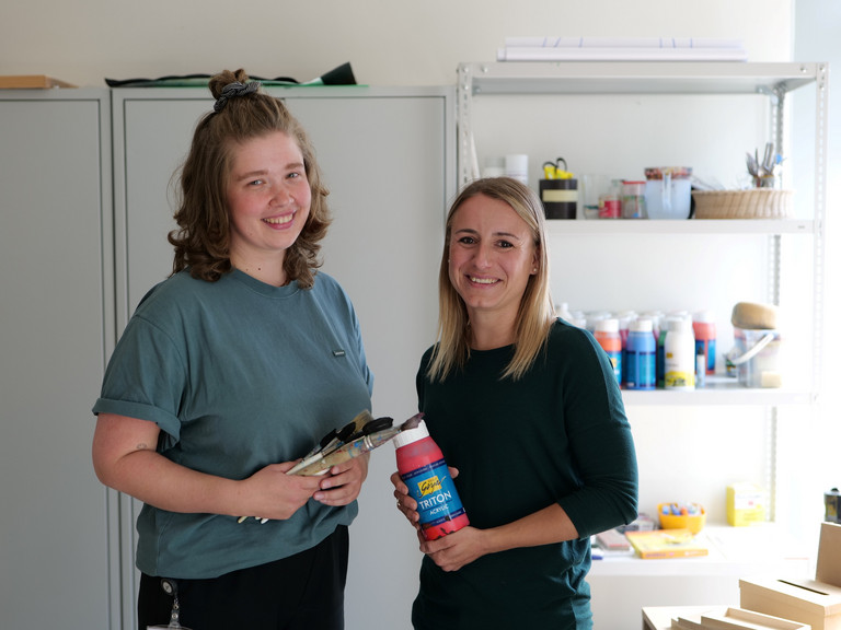Zwei Therapeutinnen stehen in einem Therapieraum mit Maluntensilien in den Händen und blicken in die Kamera im Interdisziplinären Therapiezentrum im Albertinen Krankenhaus in Hamburg