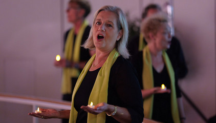 Sängerinnen und Sänger mit grünen Schals des Albertinen Mitarbeitenden Gospelchors halten LED-Teelichter in den Händen im festlich beleuchteten Kirchenraum der Kirche am Albertinen Krankenhaus in Hamburg.