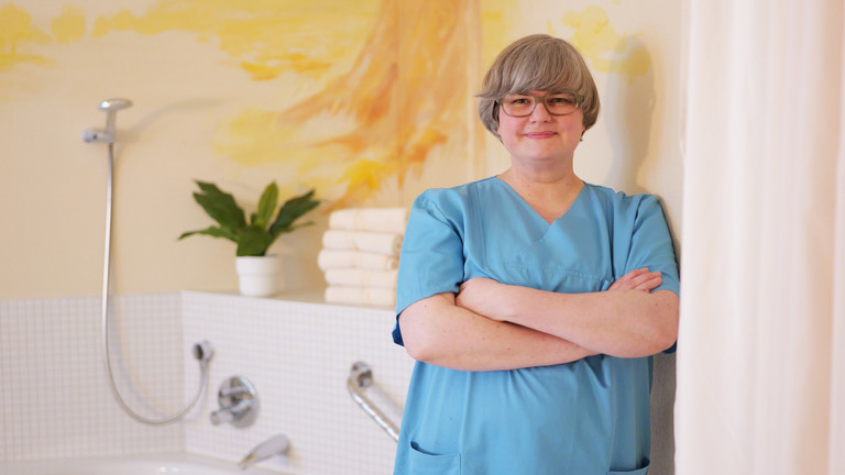 Clarissa Richter, Leitende Hebamme in der Klinik für Gynäkologie und Geburtshilfe im Albertinen Krankenhaus, steht in blauer Funktionskleidung im neuen Hebammenkreißsaal mit warmen, orangefarbenen Wandtönen und einer Geburtswanne im Hintergrund und blickt in die Kamera. Clarissa Richter, Leitende Hebamme in der Klinik für Gynäkologie und Geburtshilfe im Albertinen Krankenhaus, steht in blauer Funktionskleidung im neuen Hebammenkreißsaal mit warmen, orangefarbenen Wandtönen und einer Geburtswanne im Hintergrund und blickt in die Kamera.