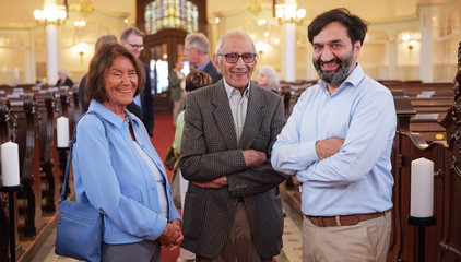 Zwei Konzertgäste stehen zusammen mit Herzchirurg Dr. Ahsannullah Madad Fassli und blicken lächelnd in die Kamera beim 10. Herzbrücke-Benefizkonzert im Hamburger „Michel“ der Albertinen-Stiftung.