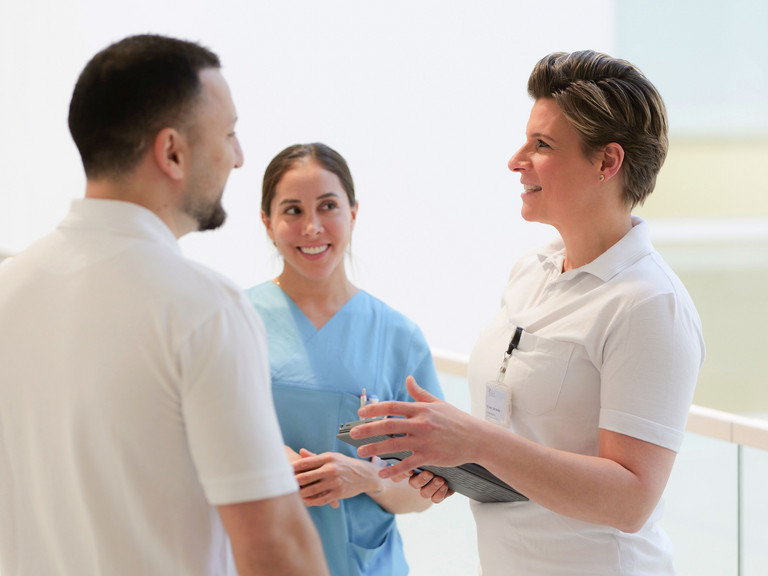 Facharzt Irakli Paatishvili und Zentrumsleiterin Dr. med. Julia M. Reinke unterhalten sich mit einer Fachpflegerin in blauer Funktionskleidung in einem Stationsflur des auf Hüftprothesen, Knieprothesen und Schulterprothesen spezialisierten Albertinen Endoprothetikzentrums Hamburg