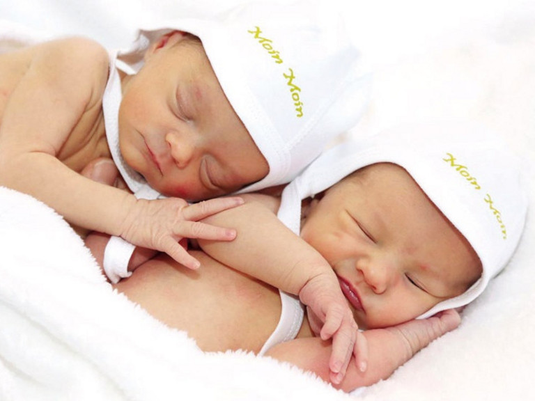 Zwei Neugeborene Babys liegen aneinandergekuschelt mkit weißenb Mützchen auf einer Decke