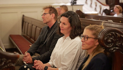 Drei Gäste sitzen auf einer Kirchenbank im Kirchensaal beim 10. Herzbrücke-Benefizkonzert im Hamburger „Michel“ der Albertinen-Stiftung.
