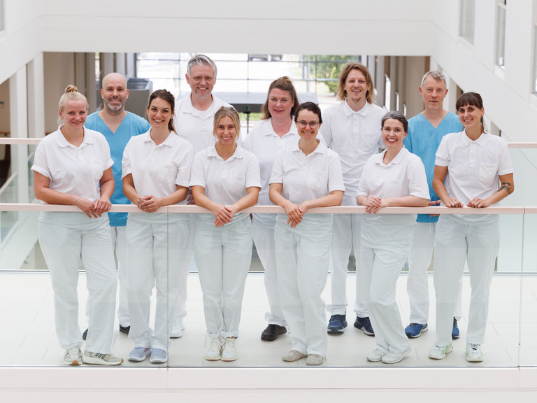 Das Team der Neurologie des Interdisziplinären Therapiezentrums im Albertinenkrankenhaus steht in Dienstkleidung freundlich in die Kamera blickend auf dem Flur