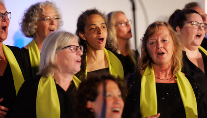 Mehrere Sängerinnen mit grünen Schals stehen nebeneinander im Chor und singen aus voller Kehle beim Konzert des Albertinen Mitarbeitenden Gospelchors in der Kirche am Albertinen Krankenhaus in Hamburg. 