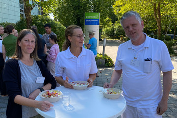 Drei Mitarbeitende des Albertinen Krankenhauses stehen bei „Let’s have lunch“ an einem Stehtisch und essen frisch zubereitete Kumpir.
