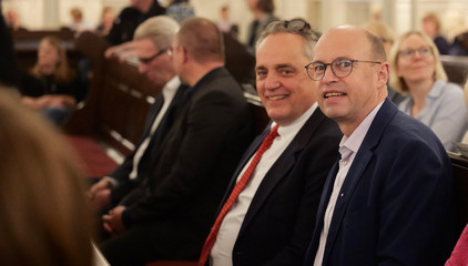 Zwei Konzertgäste sitzen auf einer Kirchenbank im Kirchensaal beim 10. Herzbrücke-Benefizkonzert im Hamburger „Michel“ der Albertinen-Stiftung.