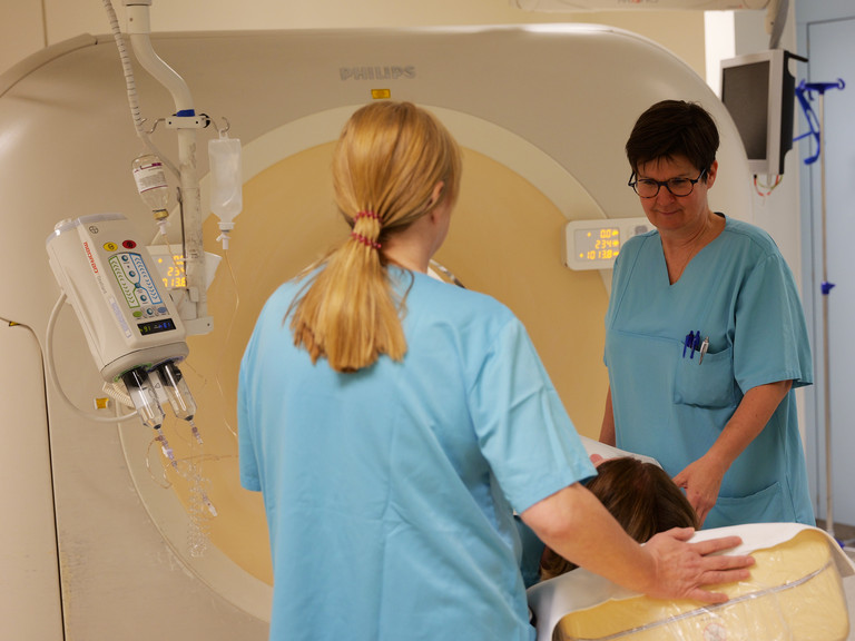 Zwei Mitarbeiterinnen betreuen eine Patientin in einem Computertomographie Gerät