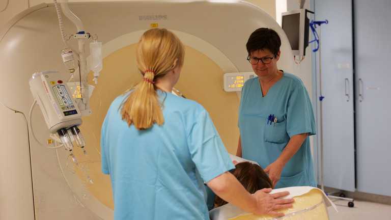 Zwei Mitarbeiterinnen betreuen eine Patientin in einem Computertomographie Gerät