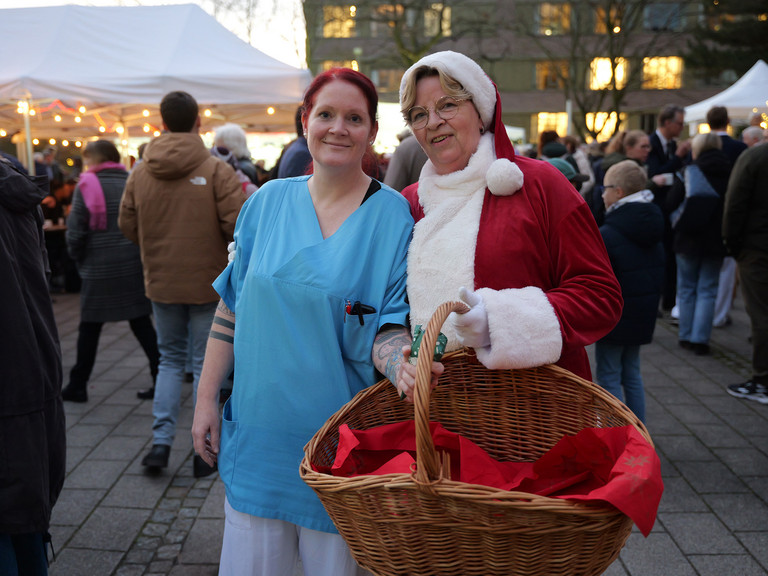 Pflegekraft und Weihnachtsfrau der Immanuel Albertinen Diakonie stehen lächelnd am Abend zusammen