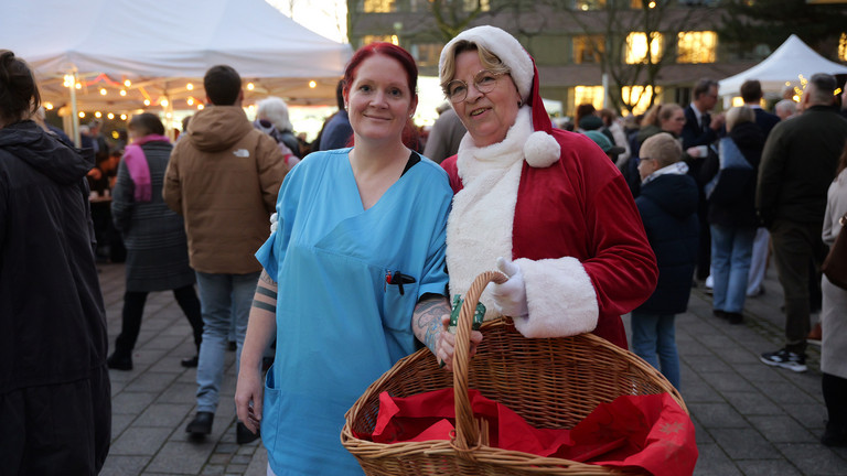 Pflegekraft und Weihnachtsfrau der Immanuel Albertinen Diakonie stehen lächelnd am Abend zusammen