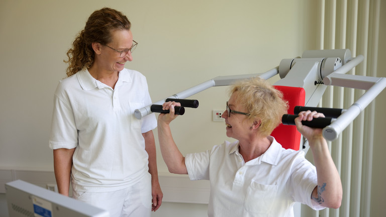 Eine Therapeutin sitzt an einem Trainingsgerät für Schulter- und Rückentraining und blickt zu einer Kollegin in weißer Arbeitskleidung im Interdisziplinären Therapiezentrum des Albertinen Krankenhauses in Hamburg Eine Therapeutin sitzt an einem Trainingsgerät für Schulter- und Rückentraining und blickt zu einer Kollegin in weißer Arbeitskleidung im Interdisziplinären Therapiezentrum des Albertinen Krankenhauses in Hamburg