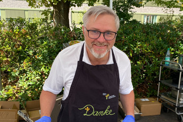 Der Ärztliche Direktor unterstützt bei „Let’s have lunch“ mit Danke-Schürze an der Essensausgabe.