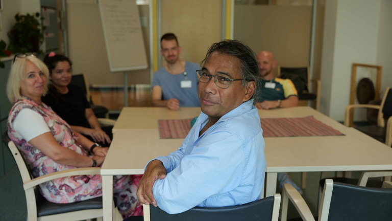 Ein Mitarbeiter blickt in die Kamera an einem Tisch mit mehreren Personen im Hintergrund bei einer Besprechung in der Klinik für Psychiatrie und Psychotherapie im Albertinen Krankenhaus in Hamburg.